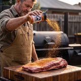 Chuds BBQ ChudRub 283g all-purpose Texas BBQ rub — a pitmaster seasoning a raw brisket from the shaker at a backyard smoker