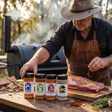 Chuds BBQ Range Bundle Texas rubs and seasonings — all four shakers on a prep bench as a pitmaster reaches for one at a cook