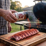 Chuds BBQ SweetCheeks 309g sweet maple BBQ rub — a cook dusting the maple rub over a rack of raw ribs on a board
