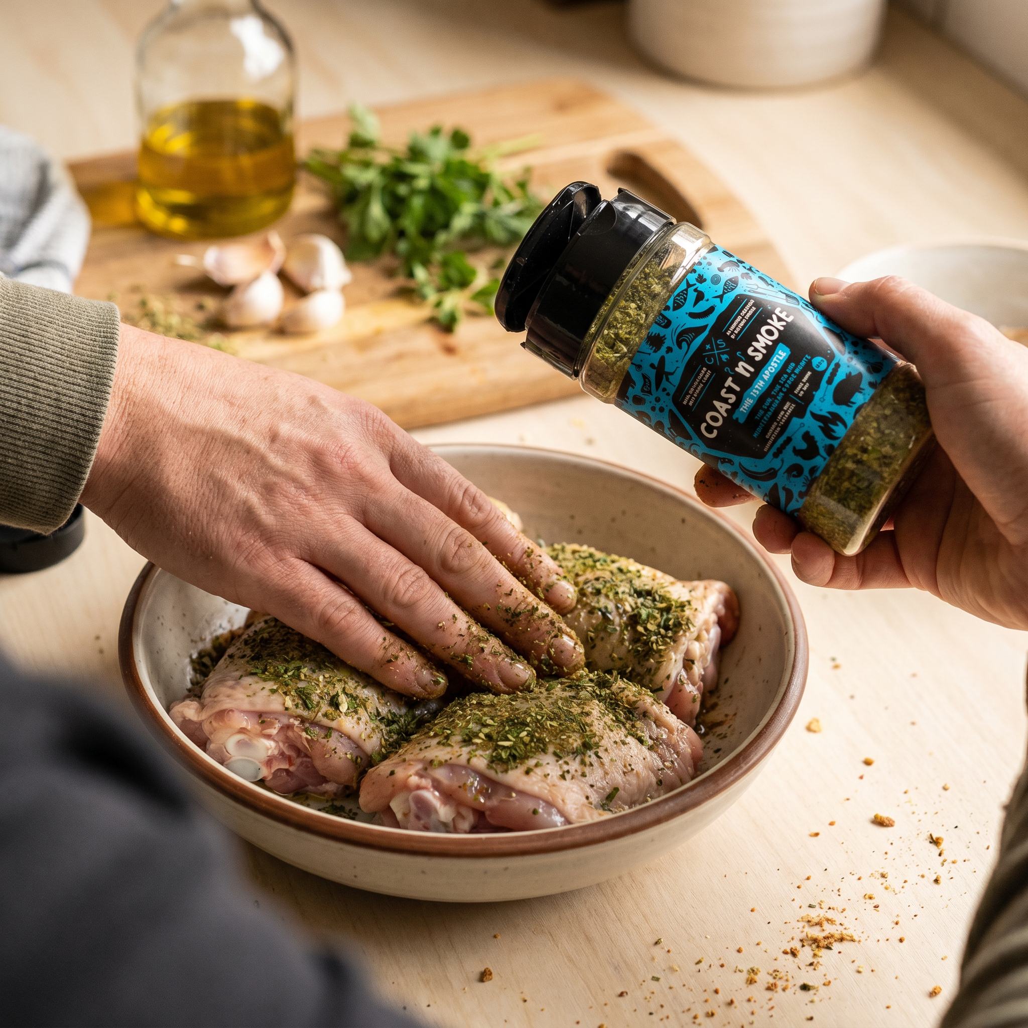 Coast n Smoke The 13th Apostle rub — cook massaging the Mediterranean herb rub into raw chicken thighs