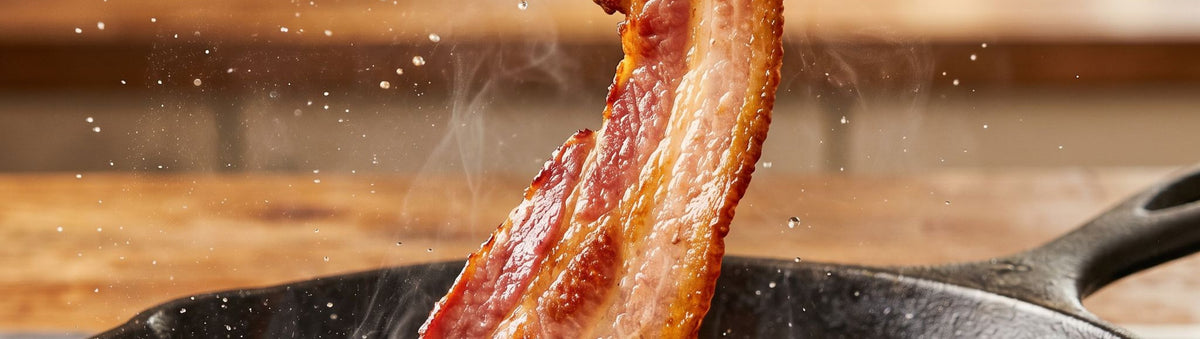 Coast n Smoke Bacon Cure banner — crispy home-cured bacon rasher lifted sizzling from the pan