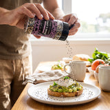 Coast n Smoke Bancoora Bagel seasoning — person sprinkling the seeded seasoning over avo toast and eggs at the table