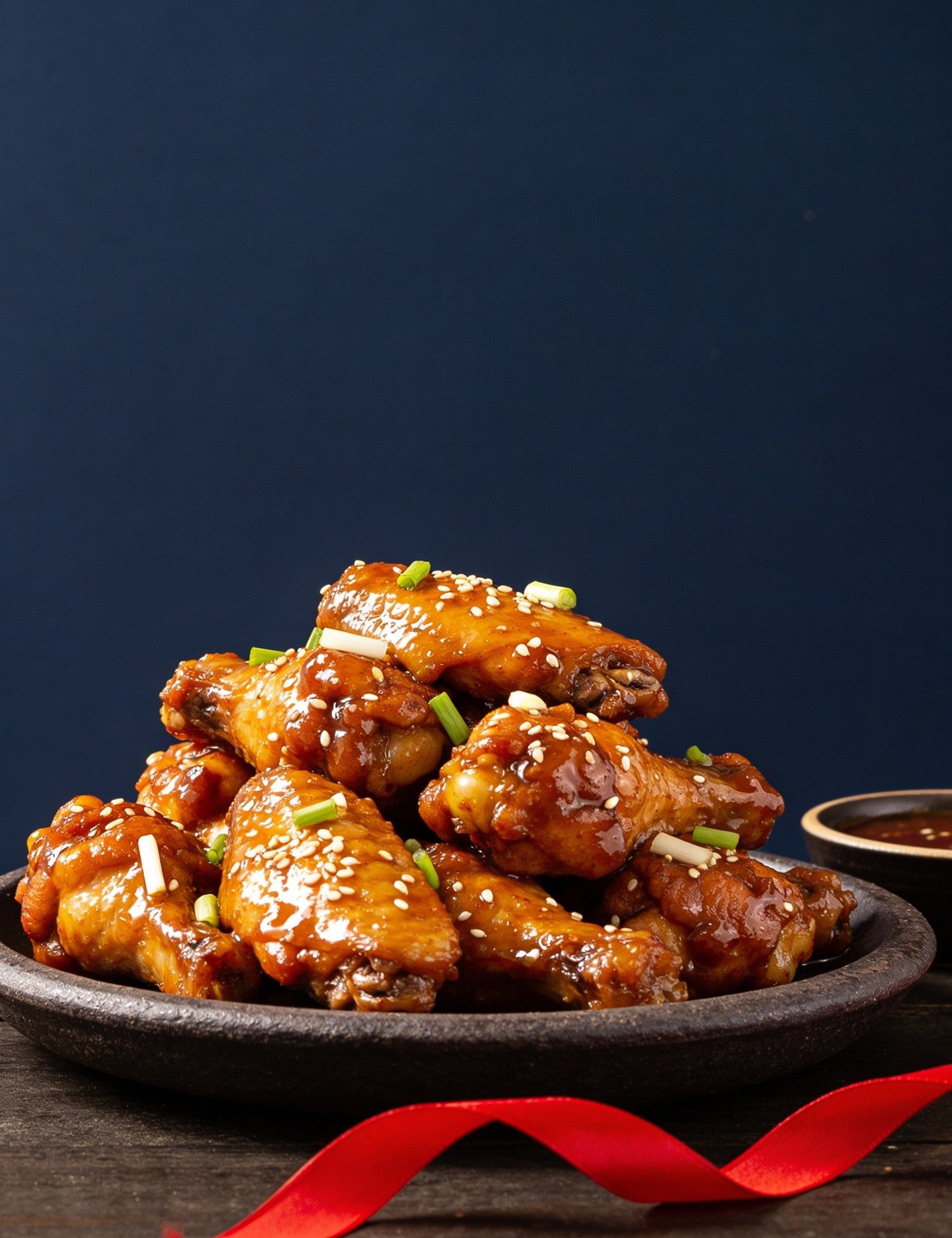 The Smuggler's Gift Crate lifestyle — platter of sticky glazed chicken wings with a red ribbon