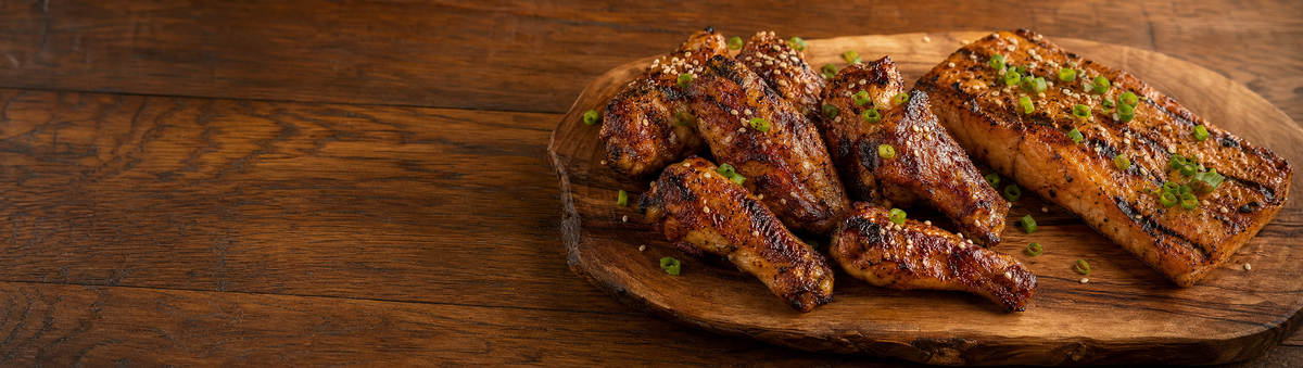 Seasoned chicken wings and grilled salmon on a platter with sesame garnish