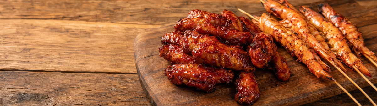 Glazed spicy chicken wings and grilled prawn skewers on a platter