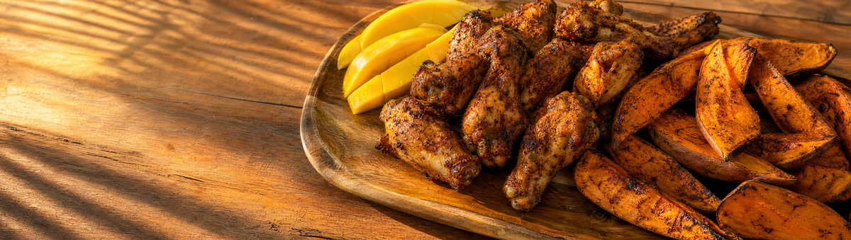 Seasoned chicken wings and roasted sweet potato with mango garnish on a platter