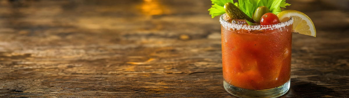 A salt-rimmed Bloody Mary cocktail glass on a rustic bar table