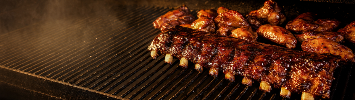 Glazed pork ribs and chicken wings with a rich amber glaze on a smoker