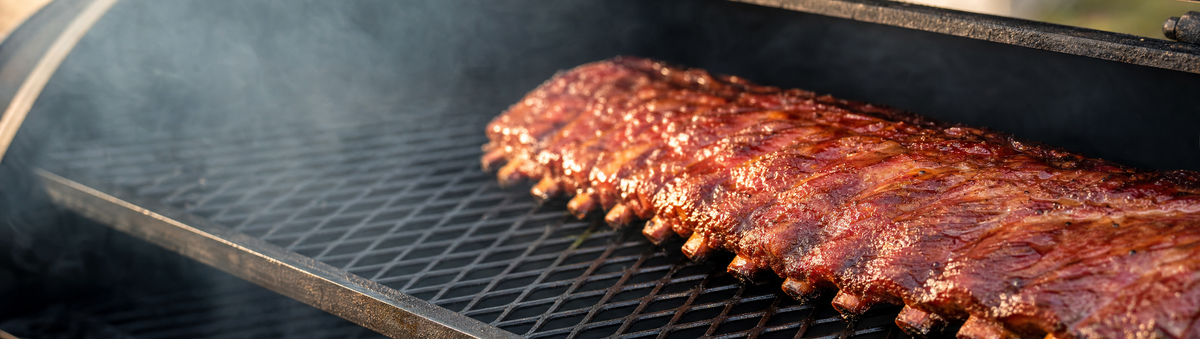 Glossy glazed pork ribs resting on a smoker at golden hour