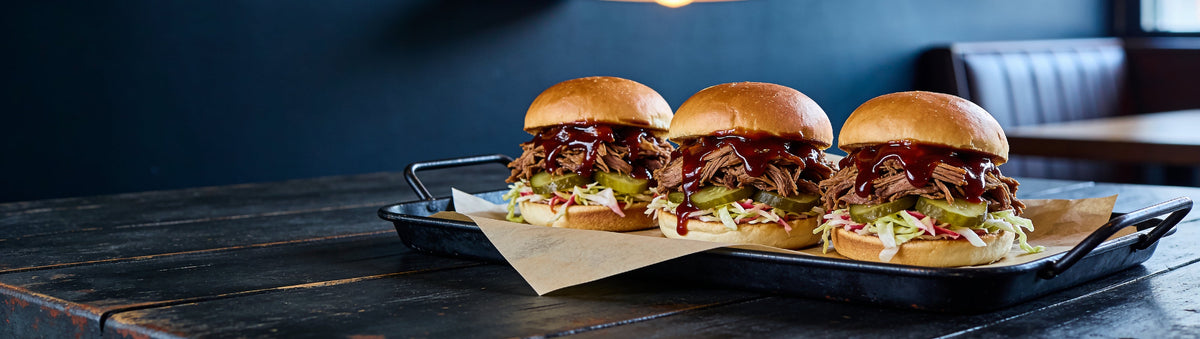 Pulled pork sliders in dark reaper BBQ sauce on a diner table – Danny Balboas Rehab