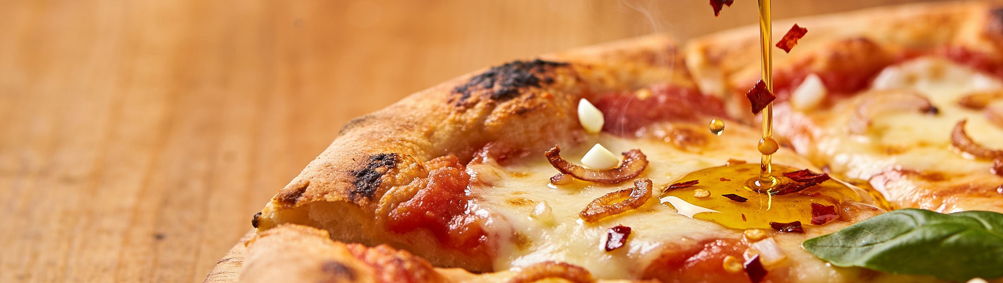 DC Cartel Olive Oil 1983 Premium Crispy Chilli Oil 268g banner - crispy chilli oil in olive oil drizzling from a spoon onto a fresh wood-fired Margherita pizza slice, oil pooling into the melted cheese with visible chilli flakes, macro shot