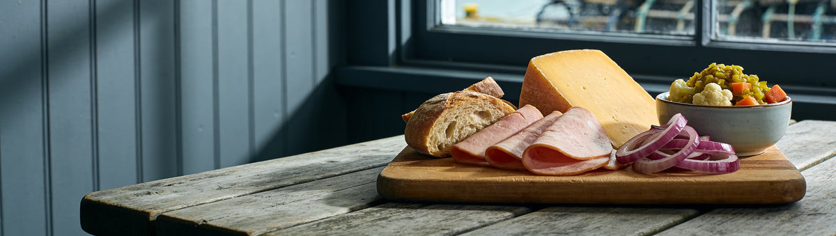 Ploughman's board with aged cheddar and ham by the harbour, served with Drunken Sailor Whisky Piccalilli