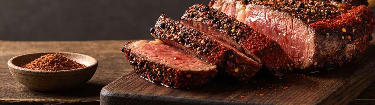 Ember Republic Lion beef rub with a sliced pepper-crusted ribeye on a walnut board