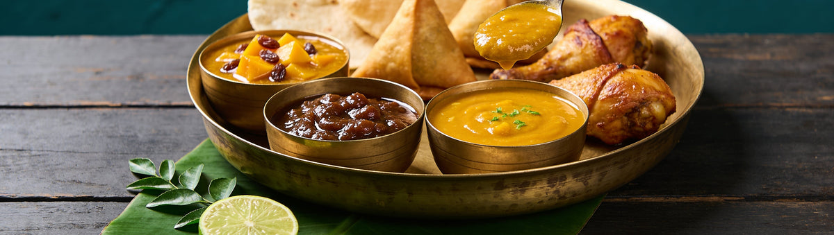 Goan Cuisine mango, tamarind and mango lime chutneys in brass bowls with samosas and roast chicken on a brass tray