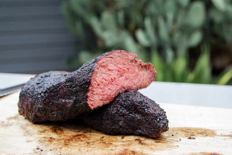 Hardcore Carnivore Black rub tri-tip, sliced open on a cutting board with an outdoor garden backdrop lifestyle photo