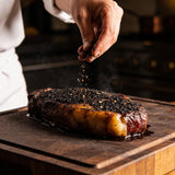 High Steaks box - charcoal black rub being sprinkled over a thick scotch fillet steak with a dark peppery crust