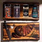 The Rub Hub High Steaks box - Steak Shooter, Black Mamba, The White Rub and The Don Steak Sauce on a timber board with a sliced scotch fillet