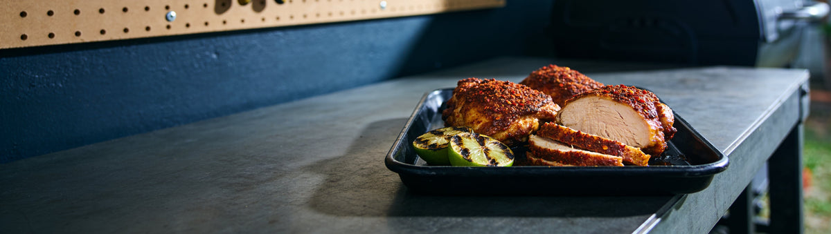 Chicken thighs crusted in KOSMOS Q Hot Dirty Bird Rub with charred limes on a workbench