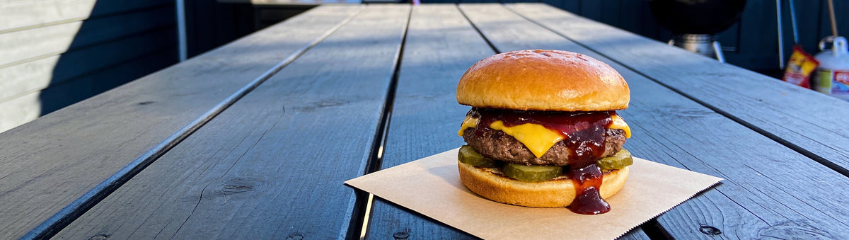 Smash cheeseburger dripping with KOSMOS Q OP-X 1 BBQ Sauce on a timber deck table