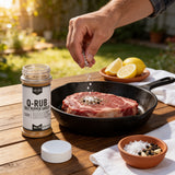 Seasoning a raw ribeye in cast iron beside Lillie's Q Q-Rub salt, pepper and garlic seasoning