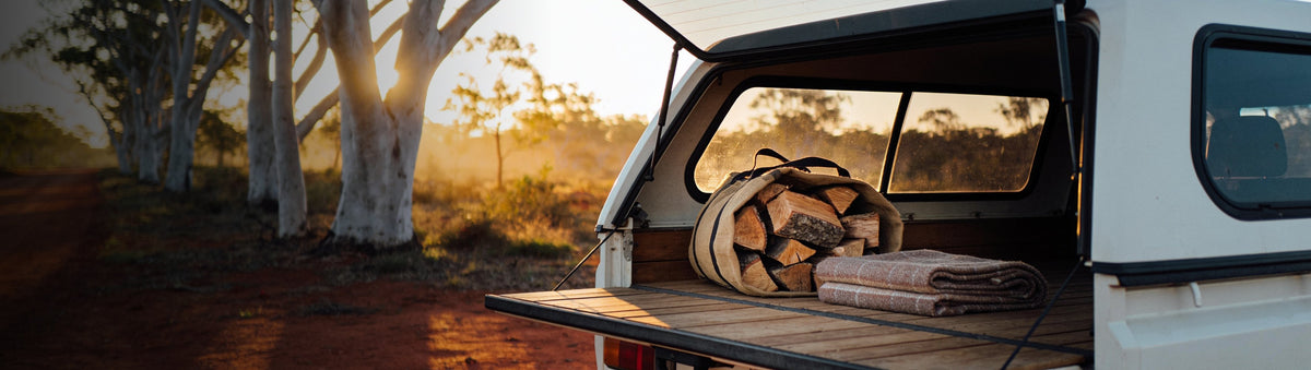 Looftlighter carry case beside a ute tailgate loaded with firewood at a red-dirt bush campsite