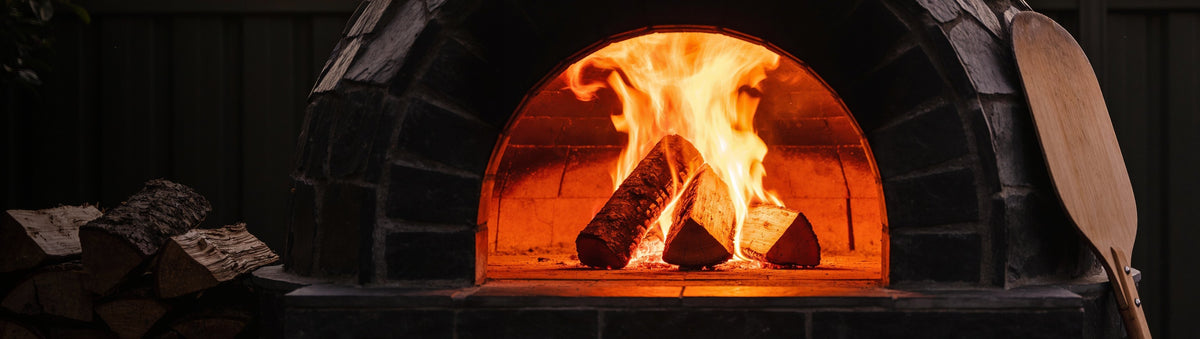 Looftlighter Pro electric fire starter beside hardwood logs catching in a backyard pizza oven