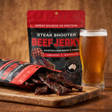Low n Slow Basics Steak Shooter beef jerky — dark beef jerky strips spilling from the pack beside a cold beer
