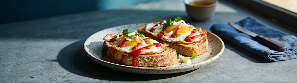 Fried eggs on sourdough toast drizzled with The Mama Hot Sauce by Mama Melisse, with coriander