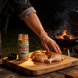 McAdventures The Adventurer BBQ Rub 200g being rubbed onto raw chicken thighs at the grill, in-use lifestyle