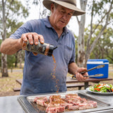 Middle Kingdom Lamb Lord 135g lamb seasoning — cook sprinkling the seasoning onto raw lamb chops at a park barbecue