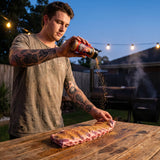 Middle Kingdom Pork Priest 170g pork seasoning — cook dusting the seasoning over a rack of raw pork ribs at a backyard table at dusk