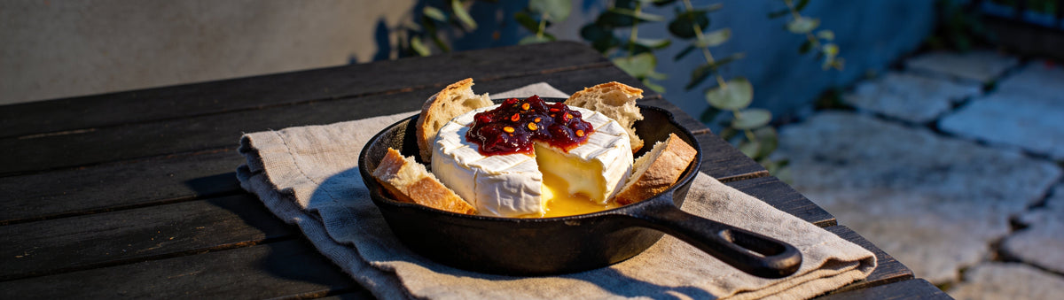 Mitch's Preserves Chilli Jam: Baked brie topped with chilli jam in a cast-iron skillet on a courtyard table