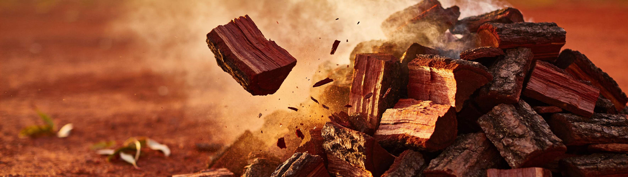 Charred ironbark wood chunks smoking gently, dense dark bark texture