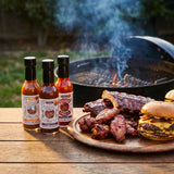 Nomad Chilli Co Barbecue Trio hot sauce bundle — three bottles beside a platter of ribs, wings and a burger by the grill