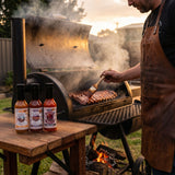Nomad Chilli Co Barbecue Trio hot sauce bundle — three bottles as a pitmaster mops ribs on a smoker at dusk