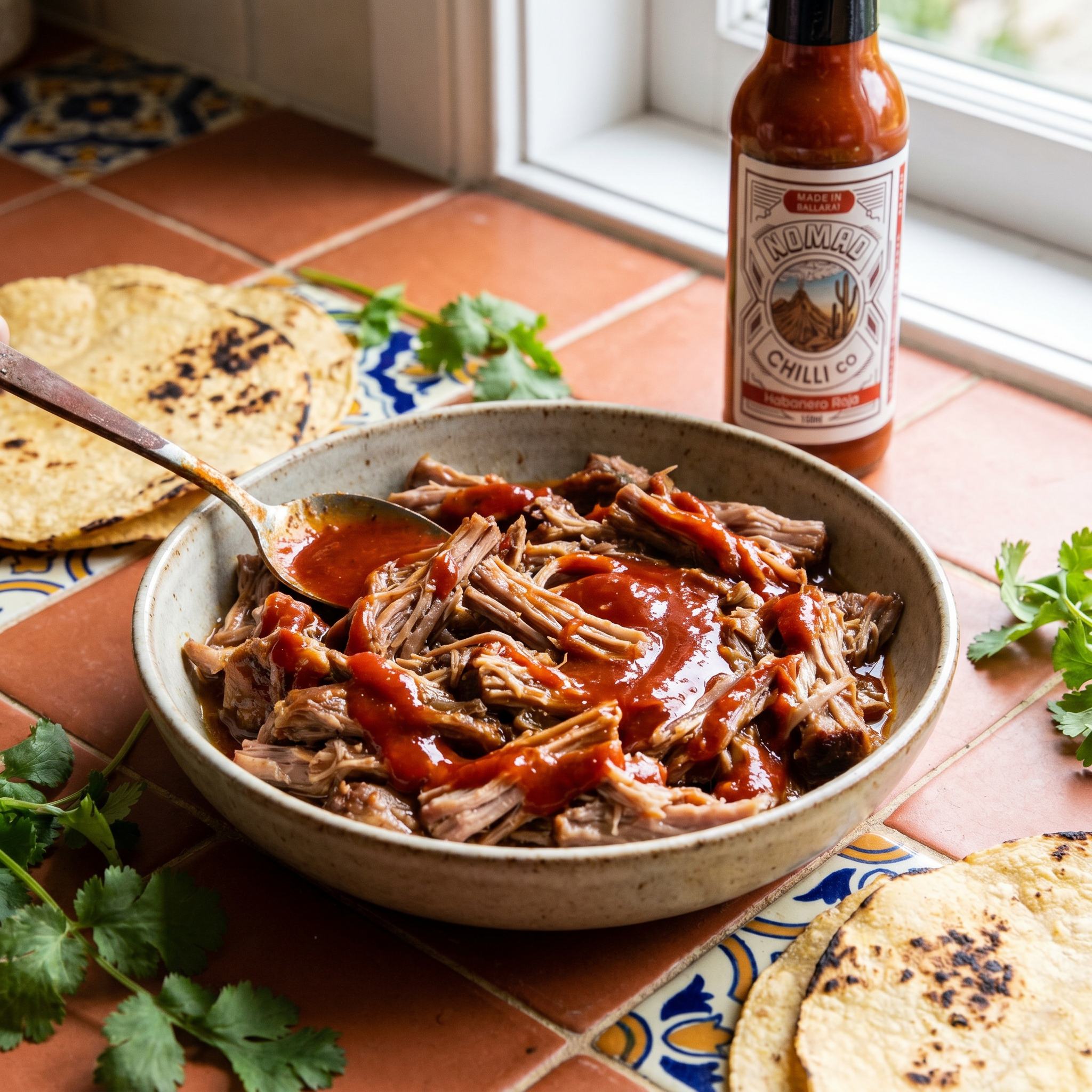 Nomad Chilli Co Habanero Roja hot sauce — slow-cooked pulled pork in a bowl with habanero sauce swirled through