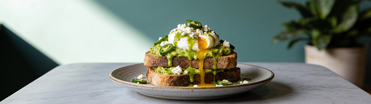 Smashed avo and poached egg with green jalapeño sauce on a marble cafe table – Old Bones Chilli Co Jalapeño & Garlic