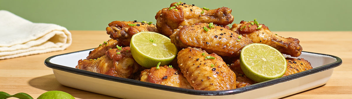 Outlaw Barbecue Lawless lime and black pepper rub with crisp chicken wings and fresh lime halves on an enamel tray