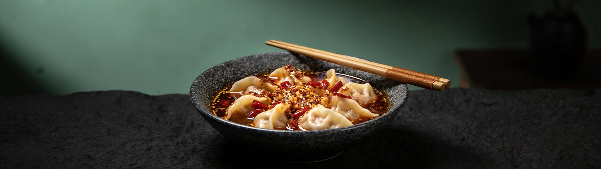 Pork dumplings spooned with Proud Phoenix & Co Hot Chilli Crisp Oil against a jade wall