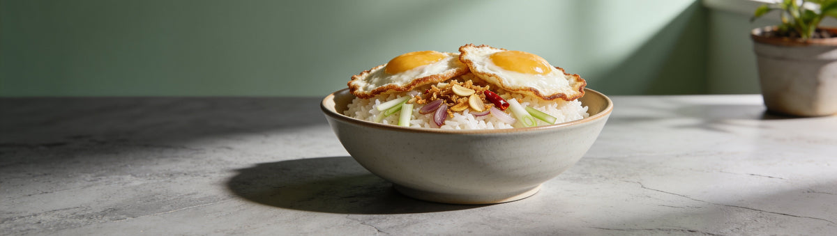 Fried eggs on rice topped with Proud Phoenix & Co Mild Chilli Crisp Oil on a stone table