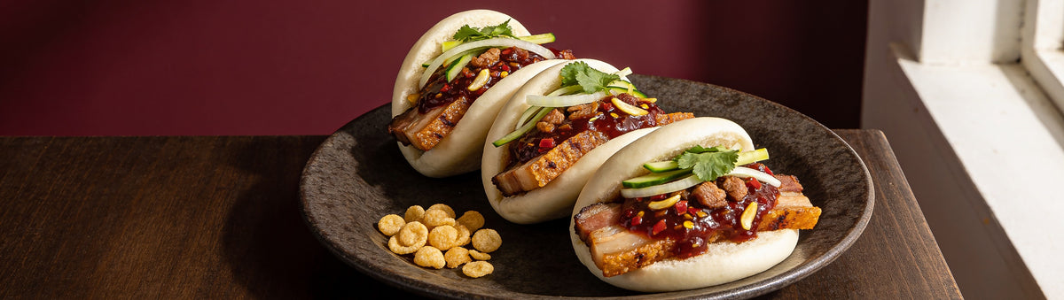 Crispy pork belly bao buns topped with Proud Phoenix & Co Pork Chilli Jam against a burgundy wall