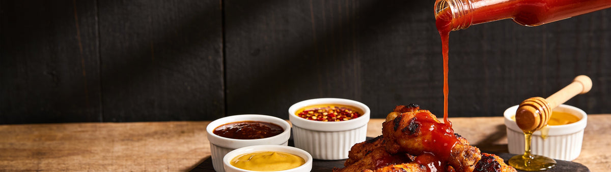 BBQ sauces and condiments: hot sauce poured over chicken wings with BBQ sauce, mustard, chilli crunch and honey