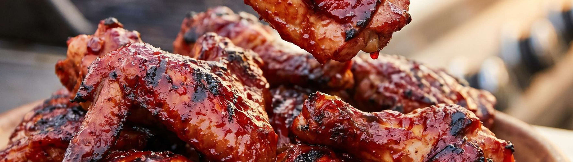 Smokes Seasoning Full Range Bundle of all five BBQ rubs beside a pile of glazed, charred BBQ chicken wings, save 20%