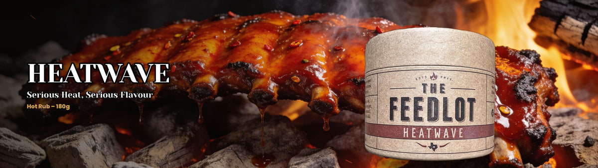 The Feedlot Heatwave Rub 180g banner — fiery glazed pork ribs dripping over hot coals