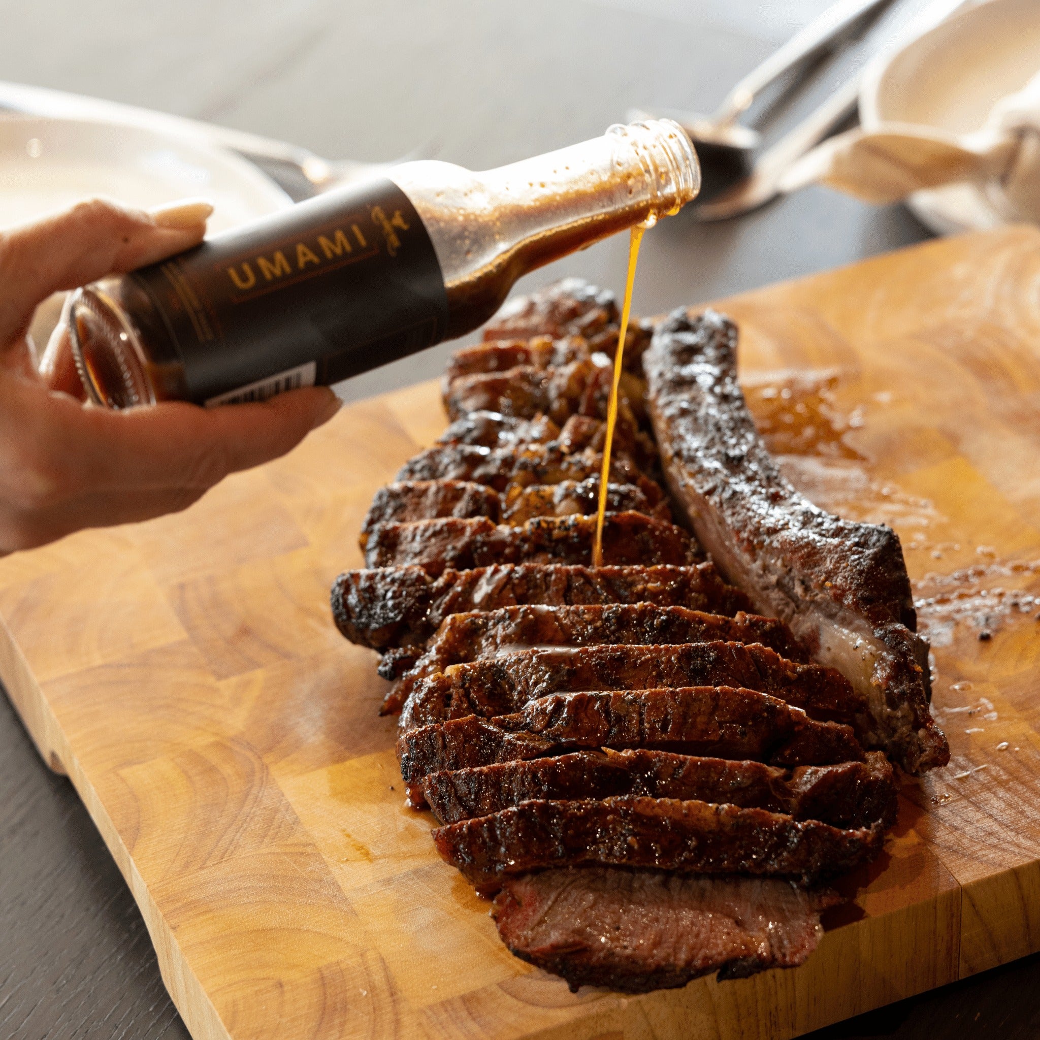 Rum and Que Umami Port & Black Garlic sauce being poured over sliced smoked beef on a board