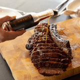 Rum and Que Umami Port & Black Garlic sauce being poured over sliced smoked beef on a board