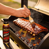 TAIPAN BBQ Competition Glaze mild sweet sticky BBQ glaze 250ml — in-use shot, brushing glaze onto ribs on the grill