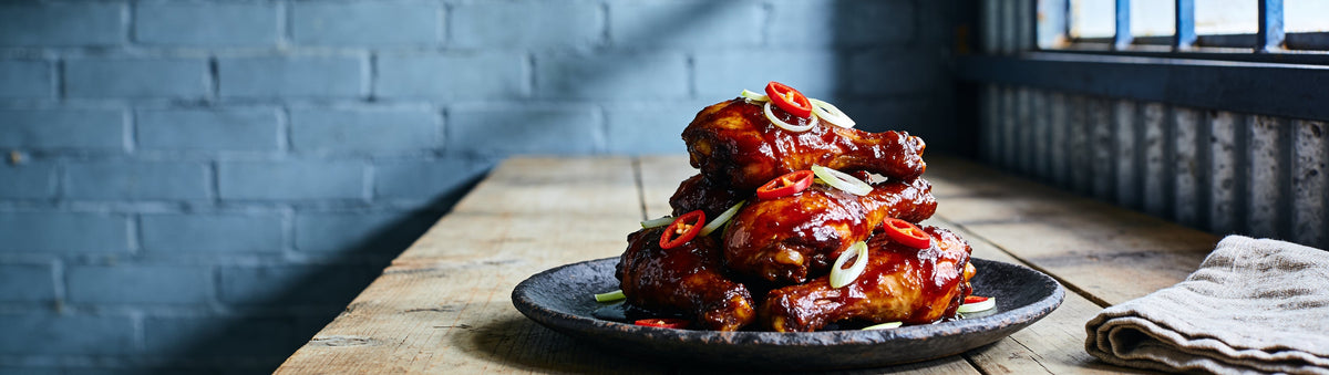 Sticky habanero-sauced chicken drumsticks with fresh chilli on stoneware – Taipan BBQ Habanero BBQ Sauce