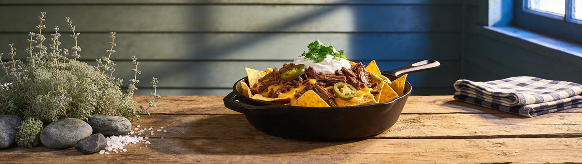 Skillet of loaded beef nachos with jalapenos on a rough timber table – Taipan BBQ Outback Fiesta