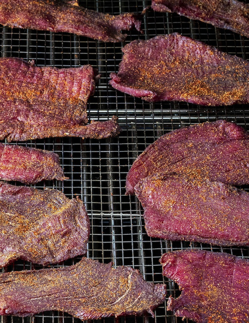 The MeatEater Outdoor Cookbook by Steven Rinella hardback cookbook — Ancho Cola Jerky drying on a rack